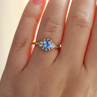 Yellow gold ring with a blue oval cut sapphire and two white trillion cut diamonds, on hand