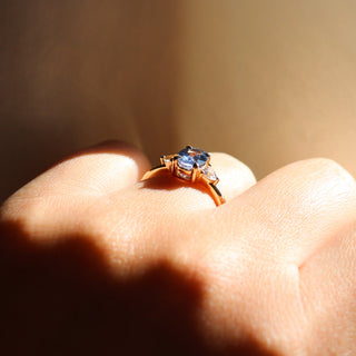 Yellow gold ring with a blue oval cut sapphire and two white trillion cut diamonds, on hand