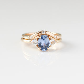 Yellow gold ring with a blue oval cut sapphire and two white trillion cut diamonds with a yellow gold curved wedding band with round white diamonds, front view
