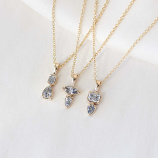Emerald and pear cut diamond necklace in yellow gold paired with diamond yellow gold necklaces on marble close up