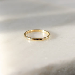Yellow gold 2mm band on white background in sunlight, front view