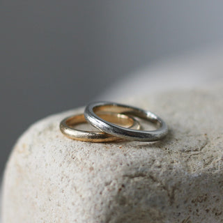 Classic Textured Thin Band in yellow gold stacked with textured white gold band on stone side quarter view