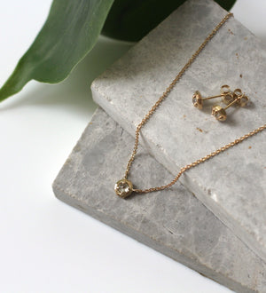 Faceted Droplet Diamond Studs paired with diamond gold necklace on stones and a green leaf