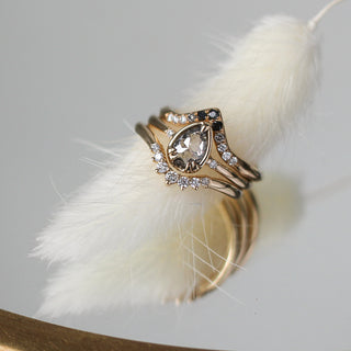 Pear cut diamond ring in yellow gold paired with 2 diamond  gold stacking bands over a feather detail front view